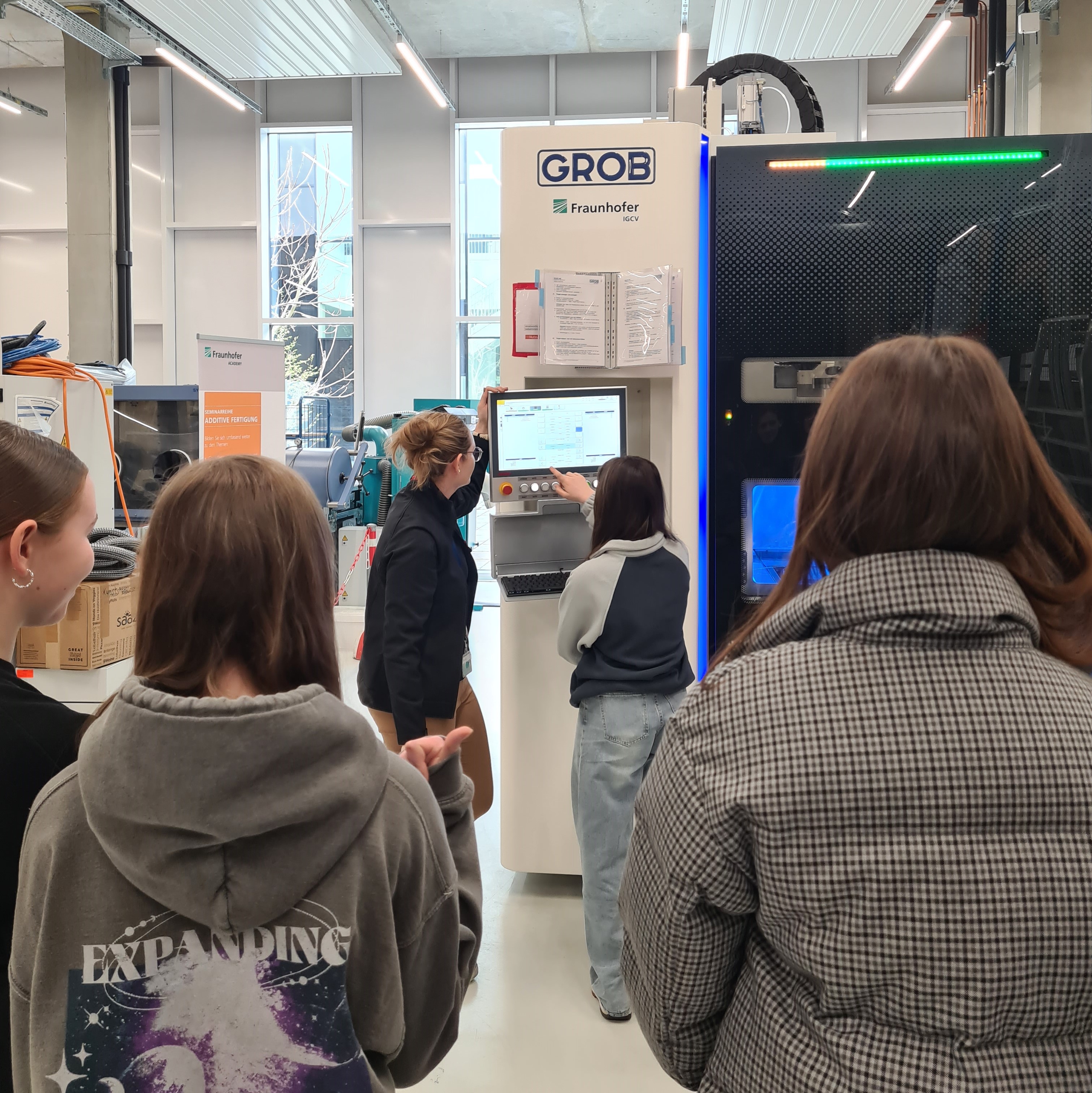 Girls watching a running AM-Machine while Julia Förster explains the process